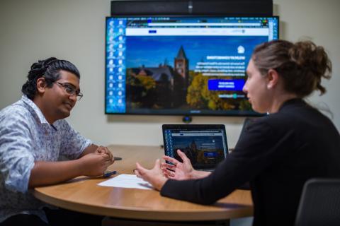 Two people discussing business with a laptop and screen at a small wooden table